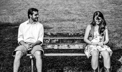 A black and white photo of a younger Reg and Kala. They are each sitting at one end of a bench. Reg is looking over at Kala and Kala is looking down.