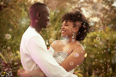 A happy bride and groom embrace while surrounded by floating bubbles at their outdoor destination wedding.