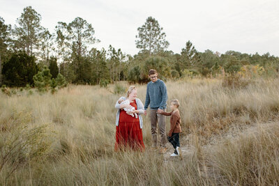 Newborn photography family photo woman holding infant with husband and child in field In Tampa Bay, Florida Nadine B Photography