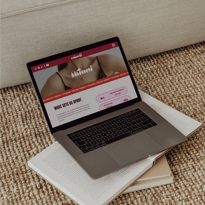 A laptop displaying the "Winett" website on its screen. The website features a minimalist design with a focus on high-quality images and a clean layout. The laptop is resting on a stack of books on a textured surface.