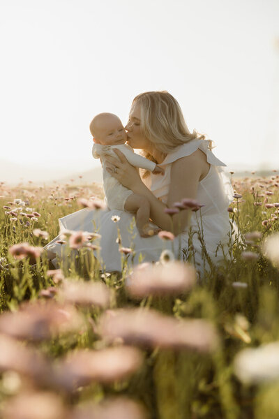 A mother sitting in a flower field during a motherhood photoshoot, super raw and loved up