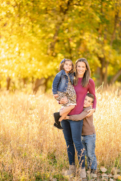 Mom hugging her young son and daughter in the fall woods by Chicago family photographer Kristen Hazelton
