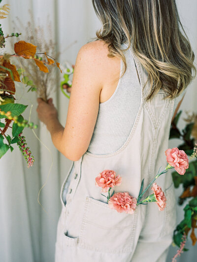 Woman with flowers in the back pocket of her tan overalls