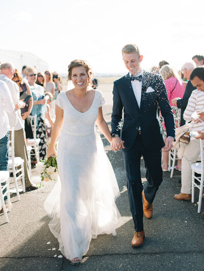Seattle wedding photographers - bride and groom smile joyfully holding hands walking down the aisle after ceremony with rice flying in air 
