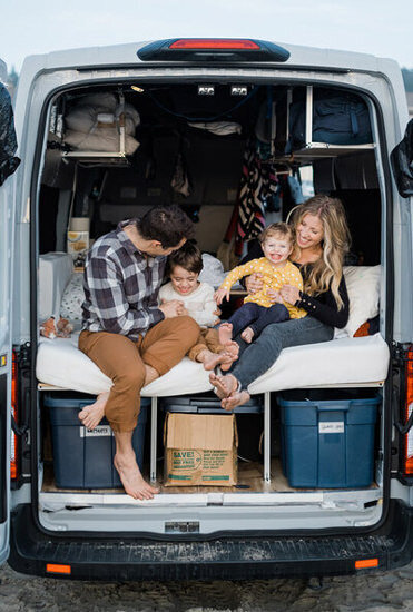 amy galbraith, an elopement photographer in washington, sits and giggles with her family in the back of her ford transit camper van