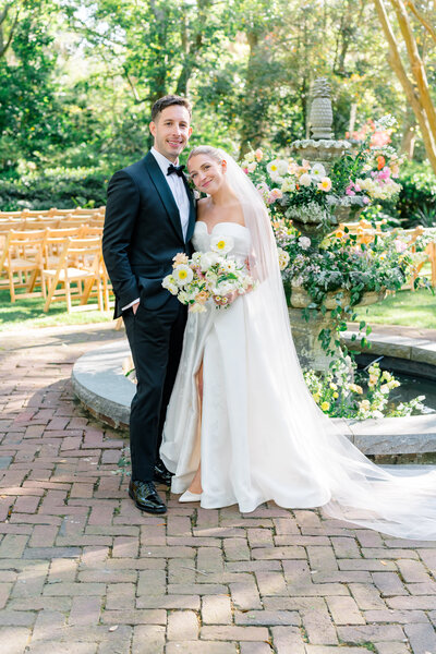 Bride and groom standing in front of fountain decorated in spring wedding flowers.
