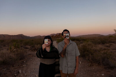 Couple holding Polaroid photos over their faces during a desert session in Utah, captured by Lamblight Photography
