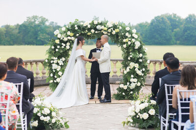 A bride and groom hold hands under their floral arch during their wedding ceremony at Great Marsh Estate