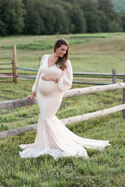 Expecting mother standing in field at sunset in maternity gown