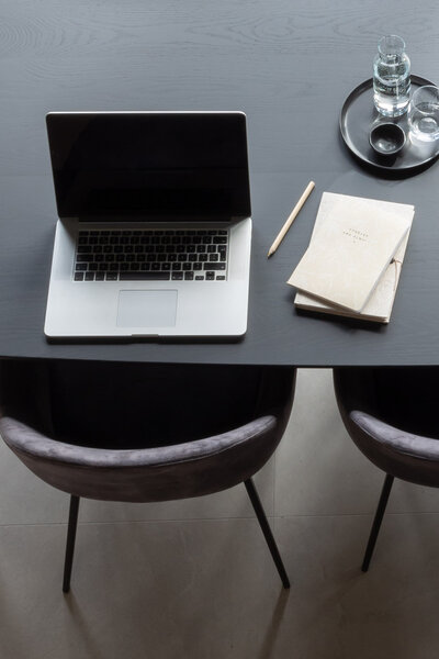 Werkplek voor mensen die voor zaken of werk naar Groningen komen. Op zwarte moderne tafel en luxe stoelen staat een geopende laptop en een notitieboekje.