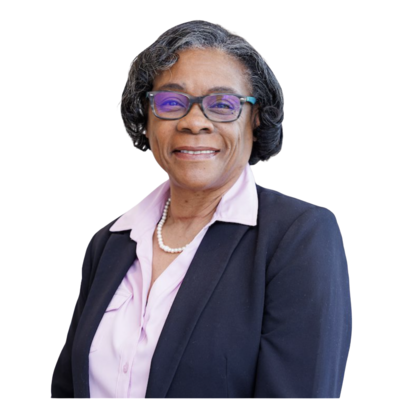 	•	“Portrait of an older woman with short, wavy gray hair, wearing purple glasses and a navy blazer over a light pink blouse. She is smiling warmly against a white background.”
