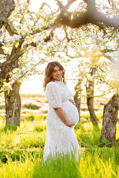 pregnant lady wearing a white dress in the cherry blossoms.