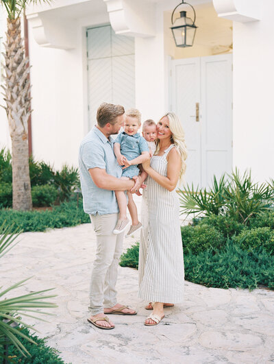 Mom and dad holding their two small children and smiling with white buildings in the background