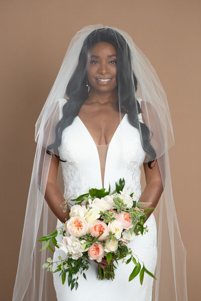 Bride wearing a cathedral length veil with blusher and holding a white and blush bouquet