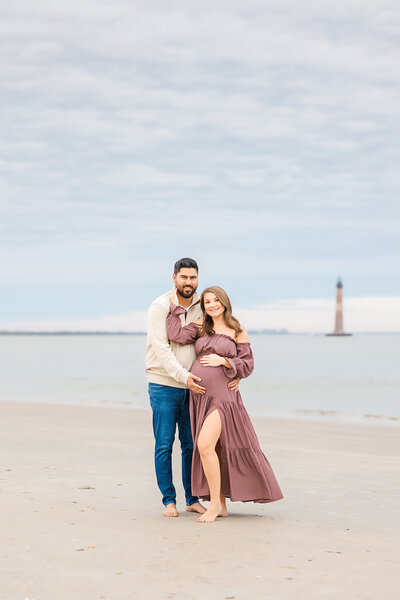 mom and dad posing holding belly at Folly Beach, South Carolina