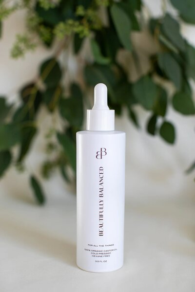 Beautifully Balanced caster oil white bottle in front of green eucalyptus 
