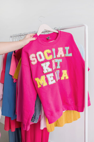 Hot pink sweatshirt with Social Kat Media in patch letters