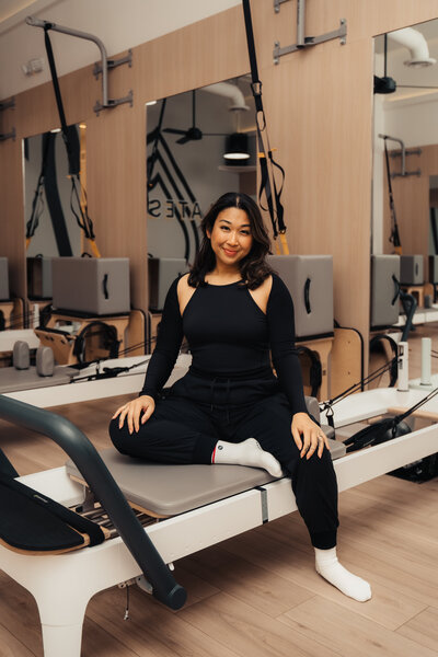Headshot of Pilates instructors Amber standing in front of Pilates214 neon logo sign.