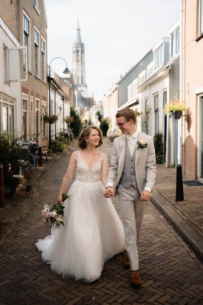 Bruid en bruidegom wandelend hand in hand in het oude stadscentrum tijdens hun bruiloft in Delft, gefotografeerd door trouwfotograaf Julia de Groot
