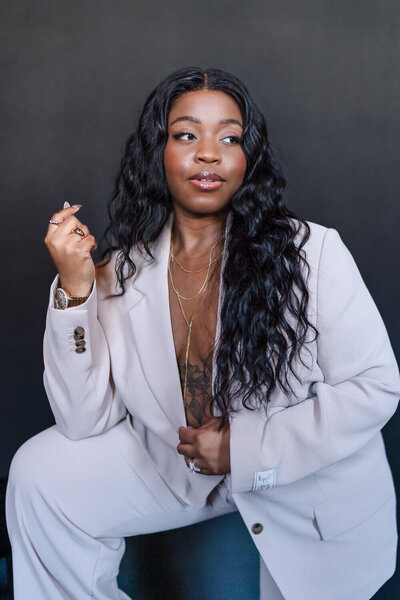 Stylish woman in a light gray suit posing confidently against a black backdrop for a professional branding photoshoot.
