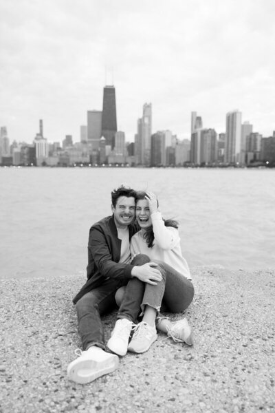 couple sit on lawn with minneapolis cityscape background in black and white image taken by tom thornton