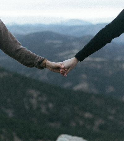 Hands reaching out towards each other with mountains in the distance.