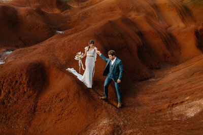 Bride and groom walking hand in hand across the red dirt ridges of Waimea Canyon during their adventurous Kauai elopement.