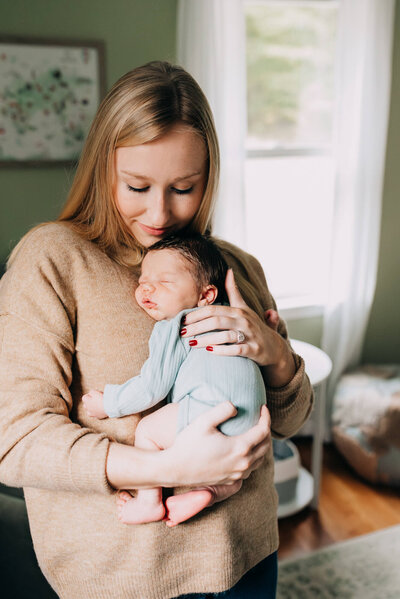 A mother holds her son against her chest in a green nursery