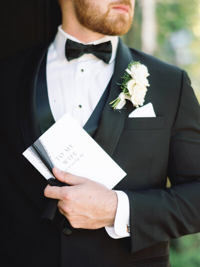 The peach orchard wedding venue groom in black tux holding vow book for his bride