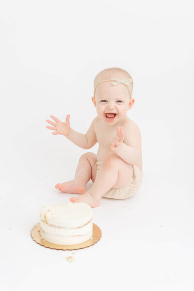 Baby girl who just turned one year old and is sitting behind a beautiful, minimal cake for her first birthday cake smash session. Neutral, white photography studio in Portland, Oregon