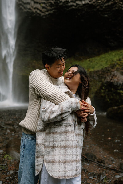 Couple embrace and laugh with eachother during their Oregon waterfal photoshoot.