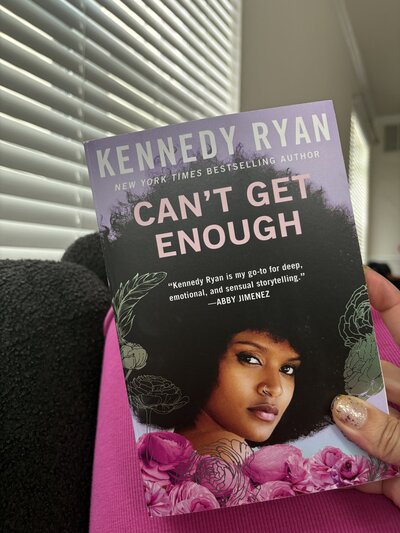 Cover of the book Cant Get Enough by Kennedy Ryan held in hand, featuring floral artwork and Black woman with natural hair. 