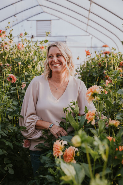 Woman smiles to her left while walking through a flower filled greenhouse