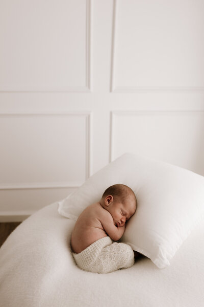 Newborn baby peacefully sleeping on white beanbag in Southwest Sydney studio with soft textures and white panelled wall background