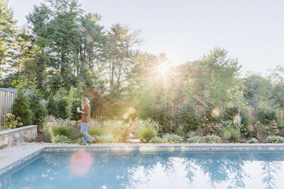 Transformed backyard with a lush garden featuring a variety of plants, trees, and ornamental grasses, creating a serene and private atmosphere around the pool, with the sun shining through the trees.