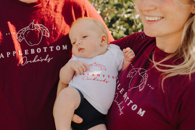 Owners, Jeff and Chelsea, holding their son while all wearing Applebottom Orchard shirts.