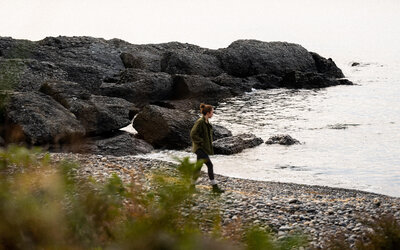 meredith ewenson walking on a costal rocky beach at sunrise wearing a green jacket