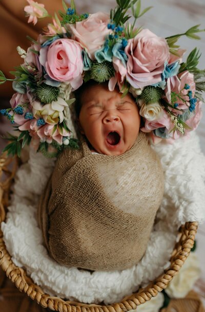 a baby wrapped in a green wrap laying in a basket for their newborn photo shoot