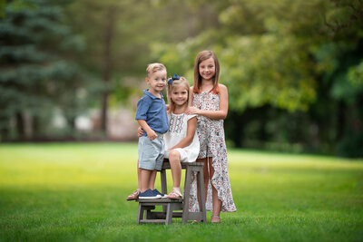 3 kids 2 girls and one by standing in the grass at their Southeast Michigan Family Photography session