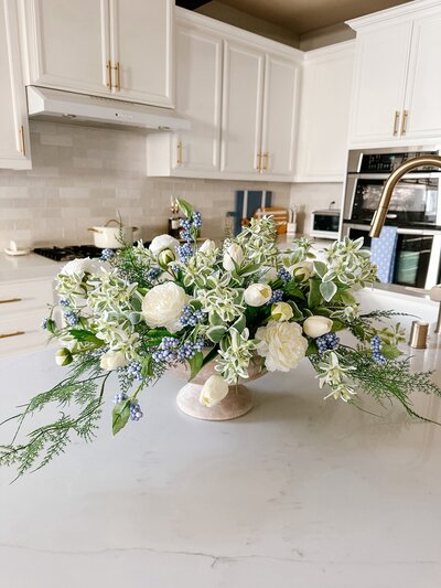 white flowers and greenery in a vase on a kitchen counter