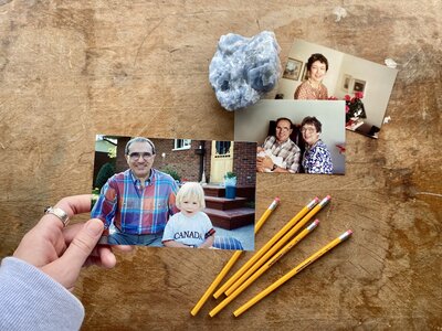 A hand holds a picture of Julian and Lauren, with other pictures and pencils scattered on the desk below.