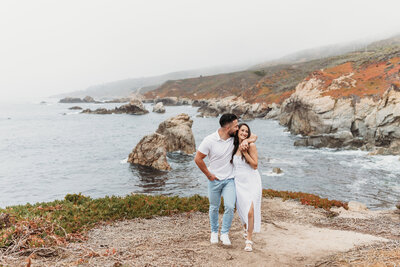 couple laughing with Big Sur cliffs in the background