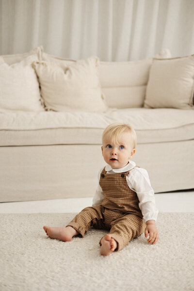A little baby boy sits on a mat in a lifestyle style milestone photoshoot in the newborn photography studio in christchurch
