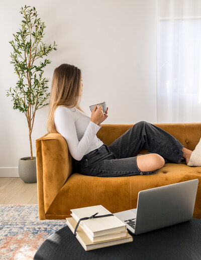 Woman sitting on a mustard couch with a cup of coffee, embracing self-reflection and living authentically.