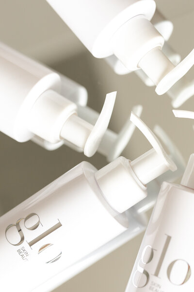 several skincare bottles are scattered about on a mirror, and this close-up photograph shows the bottle pumps