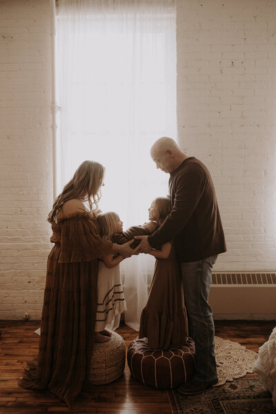 new family of five hold their newborn baby in front of the soft window light.