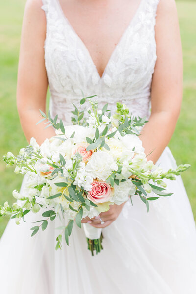 A close up detail shot of a bride holding her bouquet filled with white and pink flowers, baby's breath, and tons of greenery