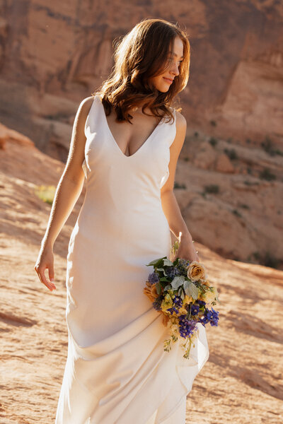 bride standing on a large rock formation while holding her bridal bouquet