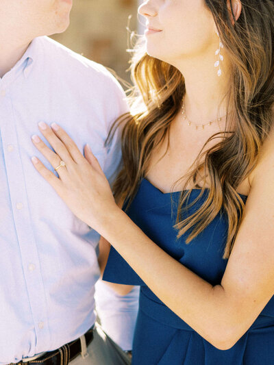 Engaged woman rests her hand on her fiance's chest and shows off her engagement ring