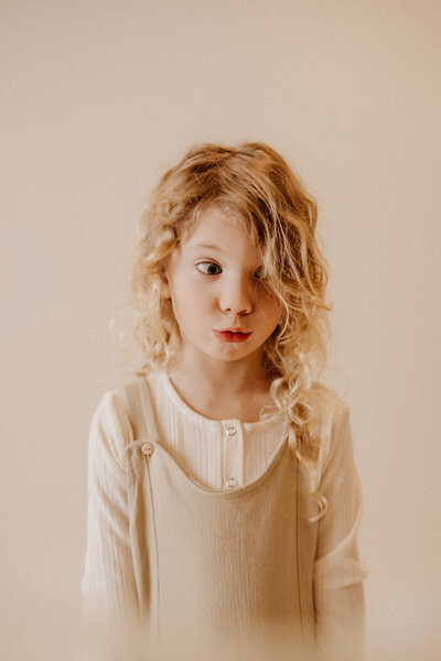 Little girl making a silly face with a beige background in the studio.